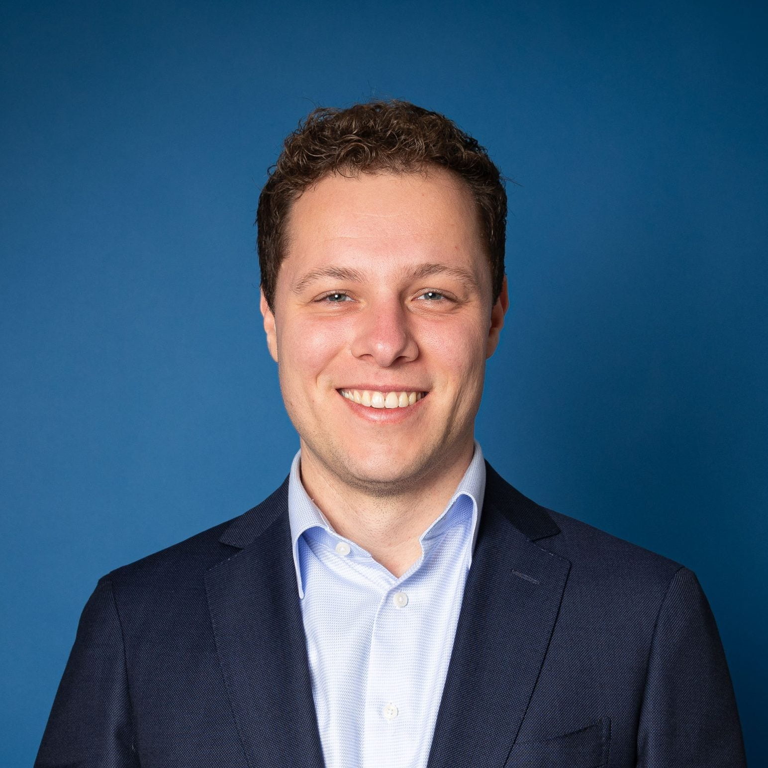 Foto van Onno James in een donkerblauw pak op een blauwe achtergrond.